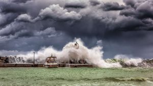 An abandoned boat anchored near a jetty is swallowed by a surging wave