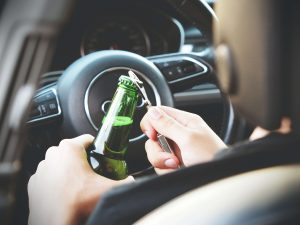 A driver uses a bottle opener to open a bottle of alcohol while driving