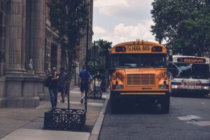 A public bus passes a school bus near a busy sidewalk