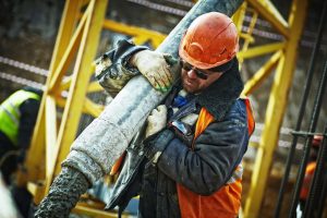 A construction worker carries a heavy section of pipe through a construction site