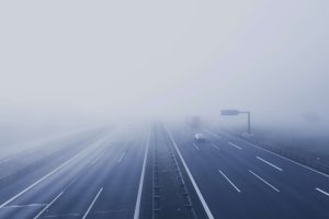 A fog-covered highway with several cars driving out of sight