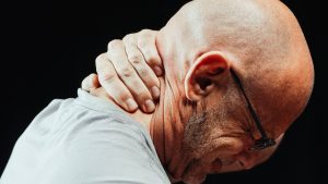 A man wearing glasses and a grey shirt holds the back of his neck, which was injured in a New Haven workplace accident
