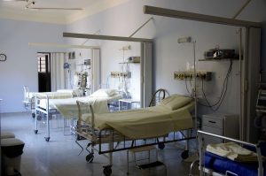 Three empty medical beds are lined up in a dimly lit hospital ward